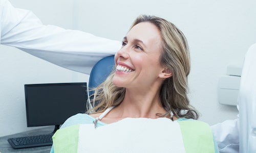 Woman smiling the dentist chair and wearing a dental bib while discussing periodontal treatment.