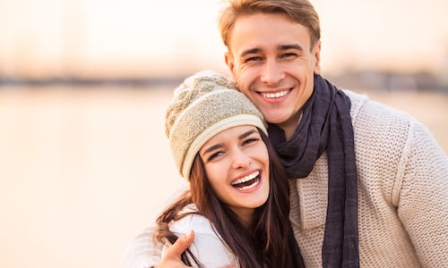Younger couple hugging outside with winter clothes on a big healthy smiles to show that we offer periodontics at our Seattle Dental office.