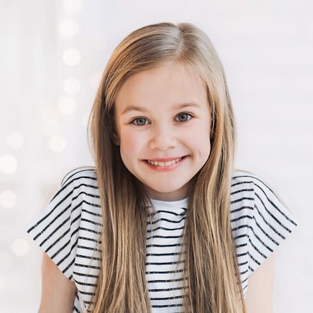 Little girl in a striped top smiling in front of a light background