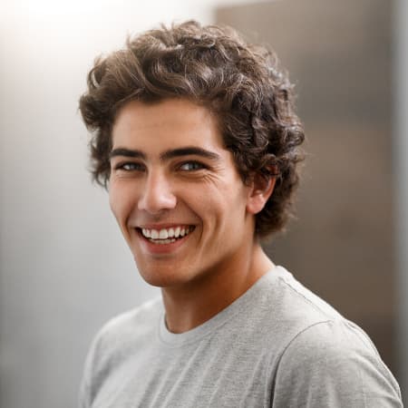 Young white man with curly brown hair in a gray t-shirt smiling after he received restorative dentistry in Seattle