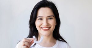 Woman smiling and holding up her clear aligner
